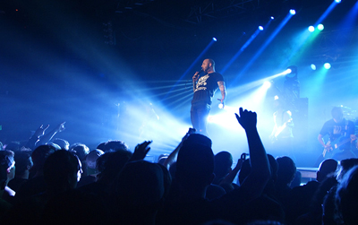 A male singer performs on a stage under bright blue spotlights in front of a crowd.