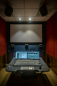 A professional audio mixing desk with dual monitors and speakers in a red-walled studio.