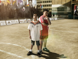 Two young boys stand on a dirt sports field with white lines under bright sunlight.