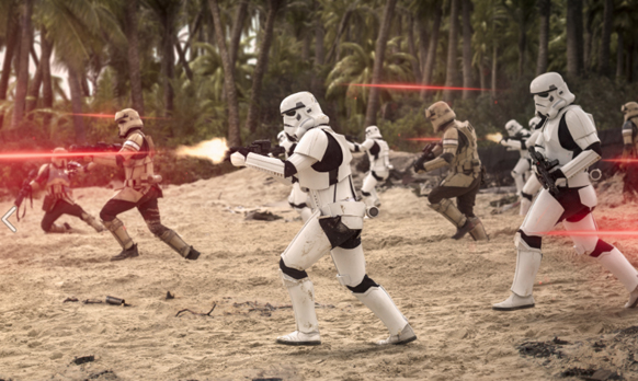 Stormtroopers and scout troopers engage in a firefight on a sandy beach with palm trees in the background.