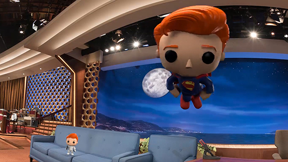 A Funko Pop Superman figure with orange hair floats in front of a studio backdrop of a moonlit ocean.