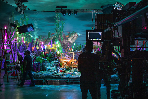 Film crew operating cameras and lighting on a colorful, artificial underwater-themed movie set.