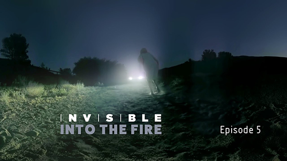 A silhouette of a person walking toward bright car headlights in a dark, grassy field at night.