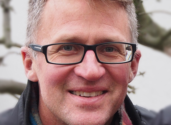 Close-up of a man with graying hair, wearing black-rimmed glasses and smiling.