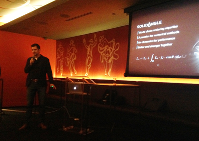 A man in a dark shirt stands next to a projection screen displaying text about SolidAngle.