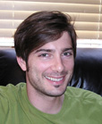 A smiling man with brown hair and a light beard wearing a green t-shirt.
