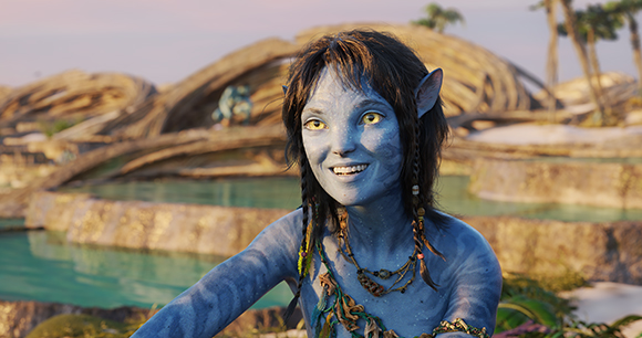 A blue-skinned Na'vi woman with dark hair and yellow eyes smiles against a tropical background.