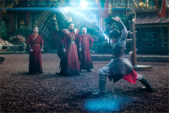 A person in grey martial arts clothing lunges toward three figures in long red robes in a courtyard.