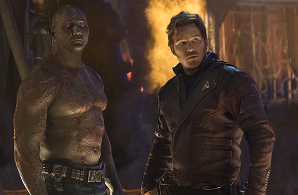A muscular, grey-skinned man with red markings stands next to a man in a dark red leather jacket.