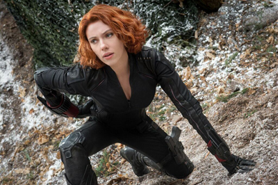 A woman with wavy red hair wearing a black tactical bodysuit crouches on a snowy, rocky hillside.