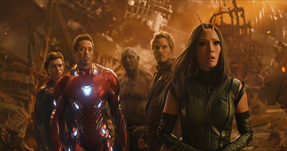 Five superheroes stand amidst smoking ruins, looking forward with serious expressions.
