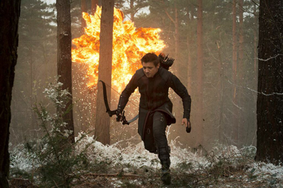 A man carrying a bow and quiver runs through a snowy forest during a large explosion.