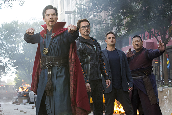 Three men in superhero costumes stand together in a city street looking toward the camera.