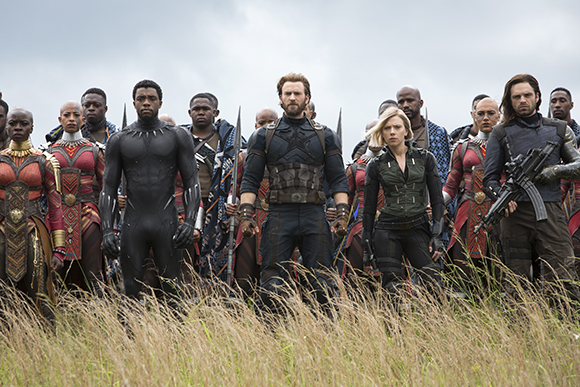 A group of diverse superheroes standing together in a grassy field under a cloudy sky.