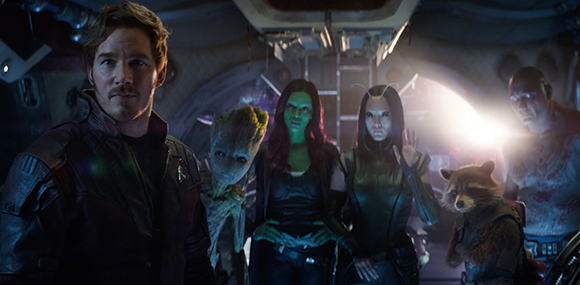 Five members of a sci-fi team stand together inside a dark, metallic spaceship.