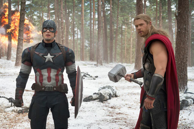 Captain America with his shield and Thor holding his hammer stand in a snowy forest near an explosion.