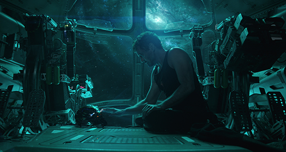 A man in a black tank top sits in a dimly lit, high-tech spaceship cockpit overlooking deep space.