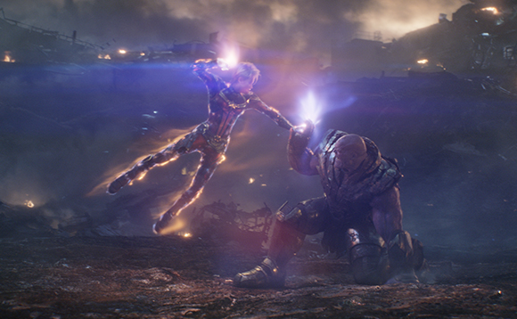 A glowing humanoid figure floats above a large, kneeling purple character in a dark, smoky battlefield.