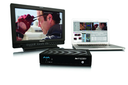 A professional video monitor showing a man's profile, a laptop with editing software, and a black hardware device.