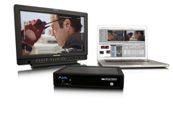 A professional video monitor, a laptop displaying editing software, and a black hardware device on a white surface.