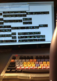 A computer monitor showing video editing software above a multi-colored editing keyboard.