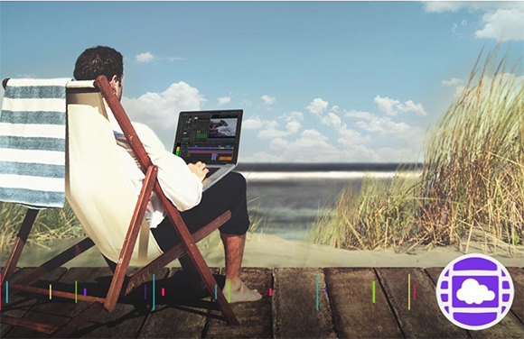 A man sits in a wooden beach chair using a laptop overlooking the ocean and sand dunes.