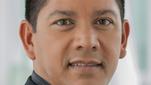 Close-up portrait of a man with dark hair and brown eyes looking forward.