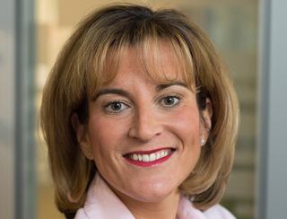 A smiling woman with shoulder-length blonde hair and bangs wearing a pink collared shirt.