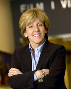 A smiling woman with blonde hair wearing a black blazer and light blue button-down shirt.
