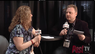 A woman with curly hair and a man in a dark jacket hold microphones during an interview.