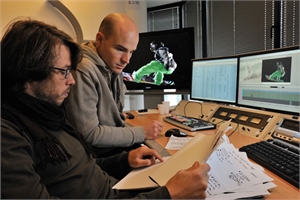 Two men review digital content and documents in a studio with multiple computer monitors.