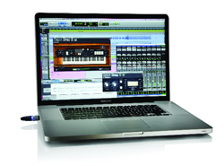 A silver laptop open on a white surface, displaying music production software with a virtual keyboard.