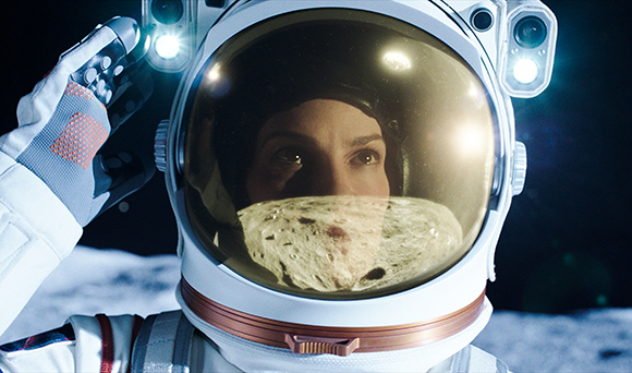 Close-up of an astronaut in a white space suit with a gold-tinted helmet visor reflecting a lunar surface.
