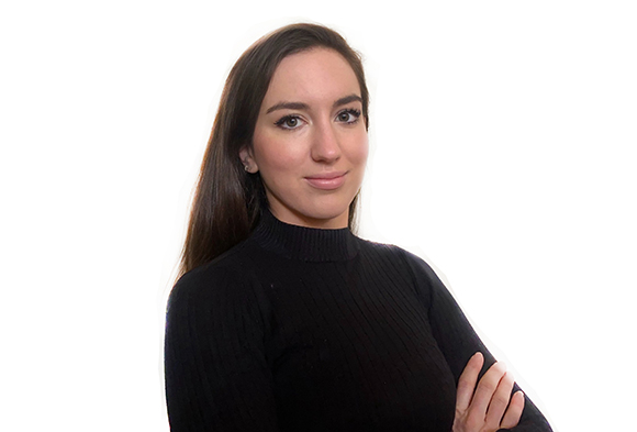 A woman with long brown hair wearing a black turtleneck, looking at the camera against a white background.