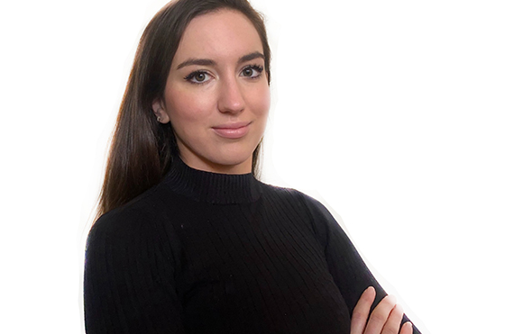 A woman with long brown hair wearing a black ribbed turtleneck, looking at the camera.