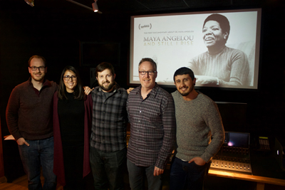 Five people stand in a dark room in front of a large screen showing a Maya Angelou documentary poster.
