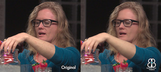 A woman with blonde hair and glasses reaches toward a glass containing red liquid and strawberries.