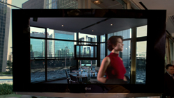 A large television screen showing a bright, modern office interior with city buildings visible through windows.