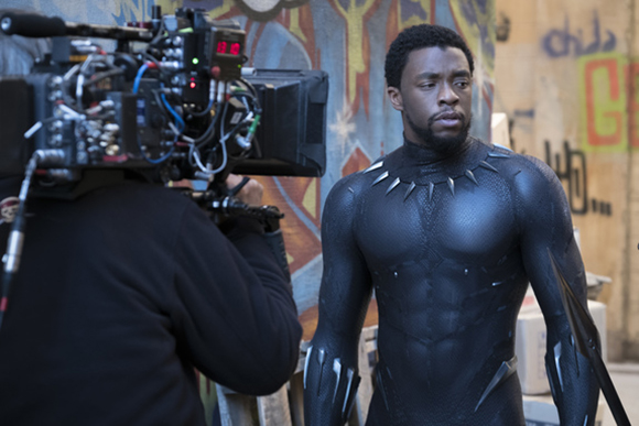 A camera operator films an actor wearing a Black Panther suit in an urban setting.