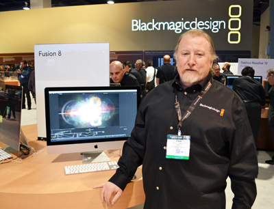 A man in a black shirt stands in front of a Blackmagic Design display featuring a computer monitor.