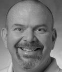 Black and white portrait of a smiling man with a bald head and a goatee.