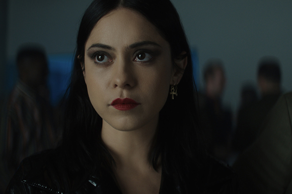 Close-up of a woman with dark hair, dark eye makeup, and red lipstick looking intensely to the side.