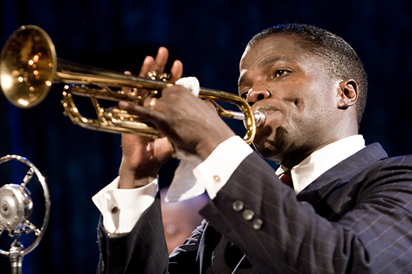 A man in a dark suit playing a brass trumpet during a performance.