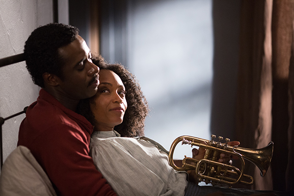 A man in a red shirt embraces a woman in a white shirt as she holds a brass trumpet.