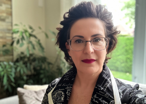A woman with short dark hair and glasses wearing a black patterned shirt.