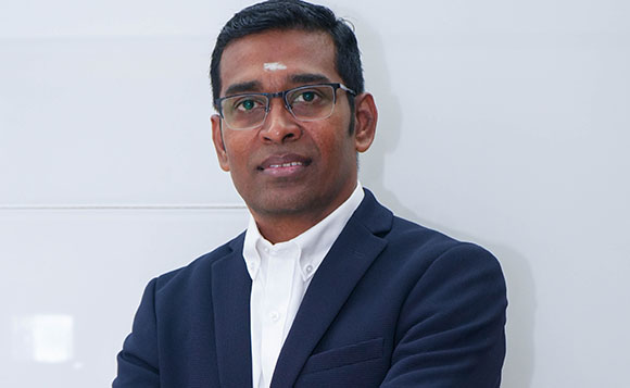 A man with glasses wearing a dark navy blazer and a white button-down shirt.