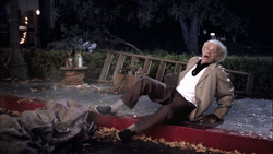 An elderly man with white hair falls backward onto a red curb at night.