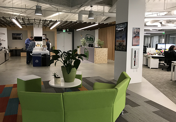 A modern office space featuring lime green modular sofas, a reception desk, and workstations in the background.