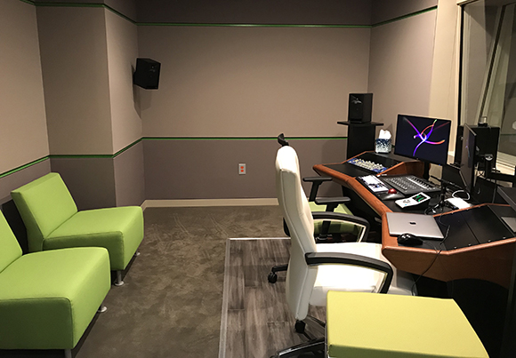A recording studio with a mixing console, computer monitors, studio monitors, and lime green lounge seating.