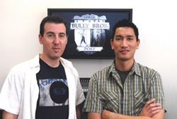 Two men posing in front of a framed Bully Bros. Post sign on a white wall.